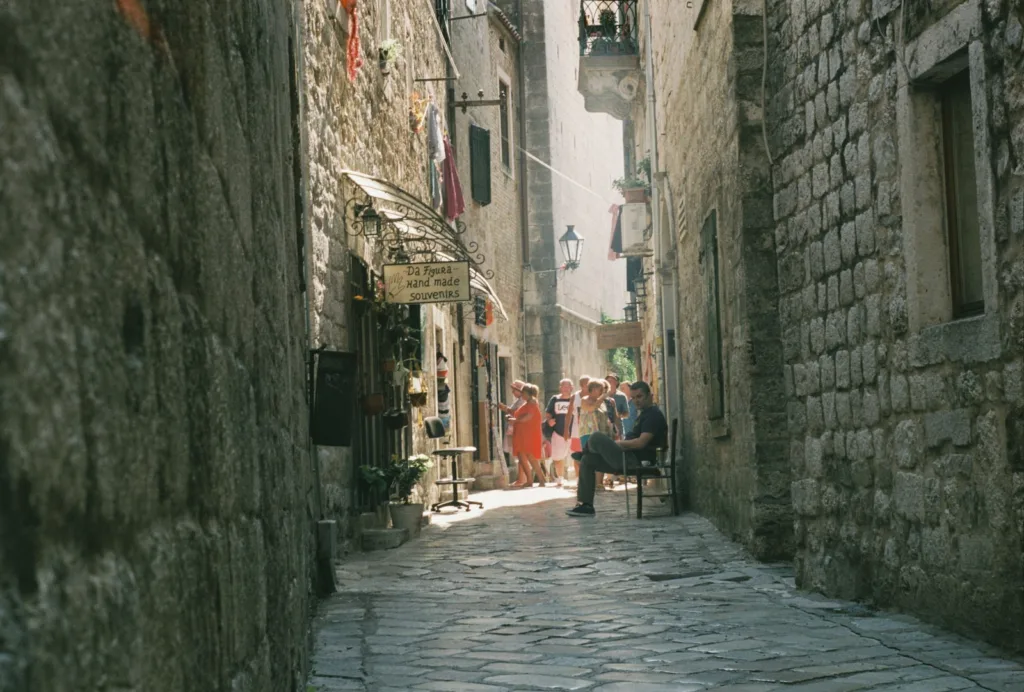 Persone che camminano lungo le antiche strade acciottolate di Kotor illuminate dalla luce del giorno.