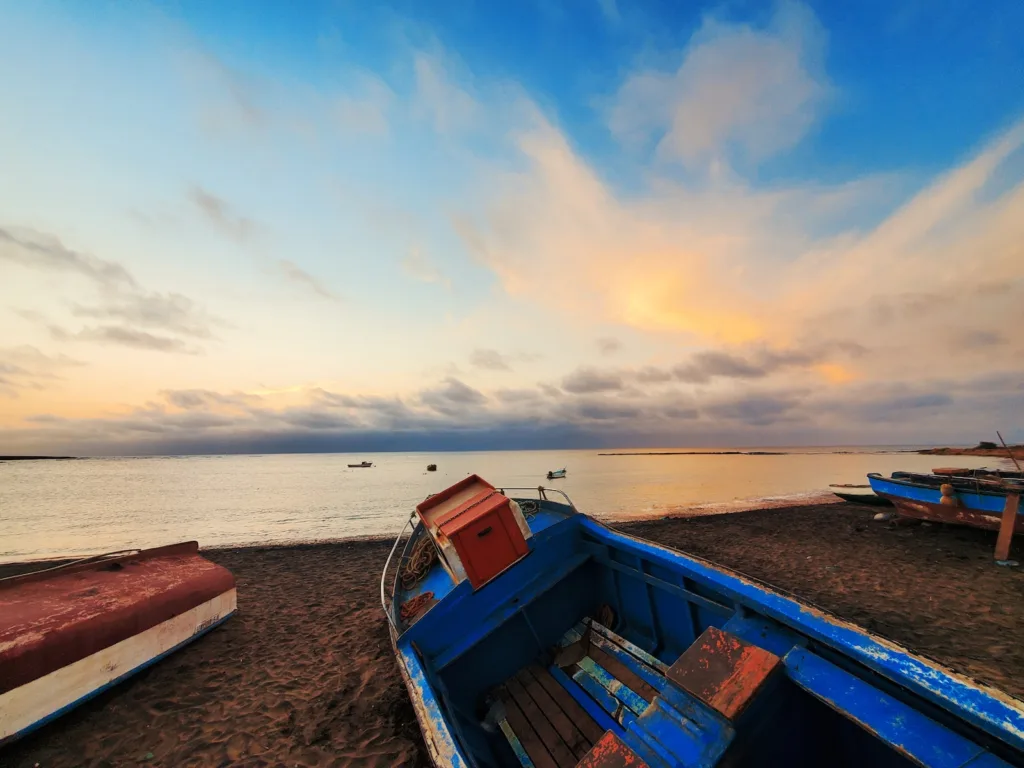 Una fotografia che cattura una vivace barca blu e rossa sulla spiaggia di Mindelo, Capo Verde, sotto il sole brillante del giorno.