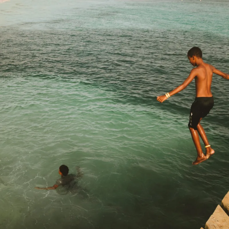 Una fotografia che cattura la gioia e la spensieratezza di un gruppo di ragazzi che si godono il bagno nelle acque turchesi di Mindelo, Capo Verde.