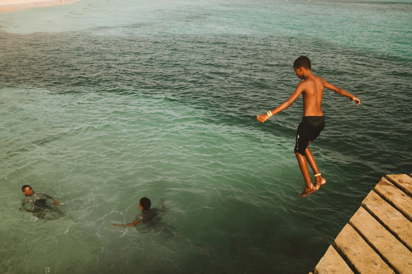 Una fotografia che cattura la gioia e la spensieratezza di un gruppo di ragazzi che si godono il bagno nelle acque turchesi di Mindelo, Capo Verde.